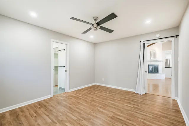 a view of an empty room with wooden floor and a ceiling fan