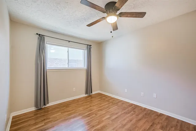 an empty room with wooden floor ceiling fan and window