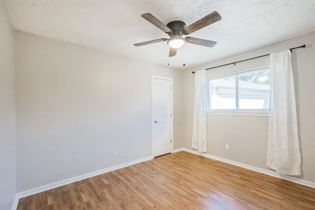 an empty room with wooden floor ceiling fan and windows