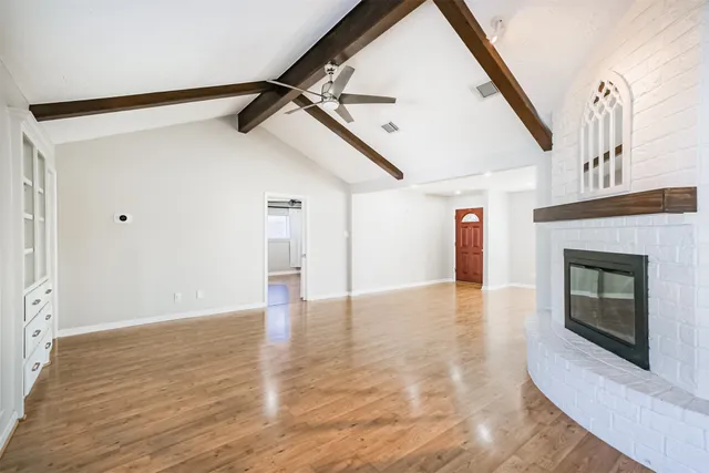 a view of an empty room with wooden floor fireplace and a window