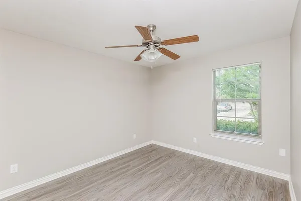 an empty room with wooden floor ceiling fan and windows
