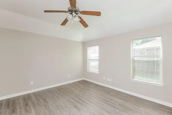 an empty room with wooden floor fan and windows