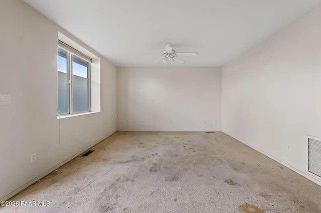 an empty room with a chandelier fan and windows
