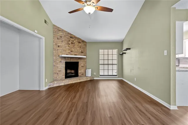 an empty room with wooden floor fireplace and windows