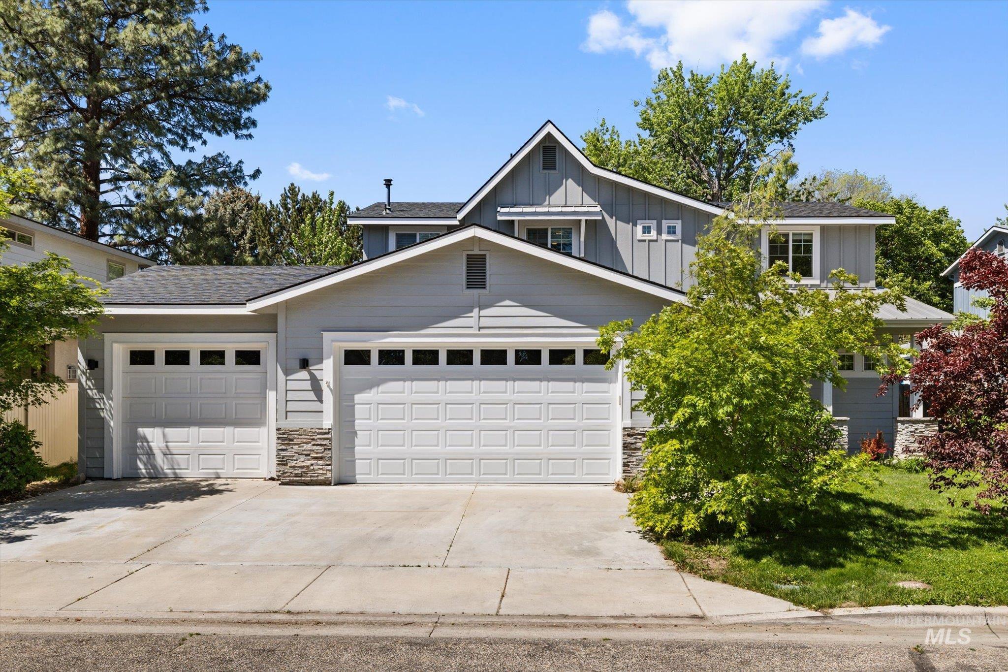 Contemporary residence featuring light gray siding with stone accents, a multi-gabled roofline, and a three-car garage with panel doors and window inserts