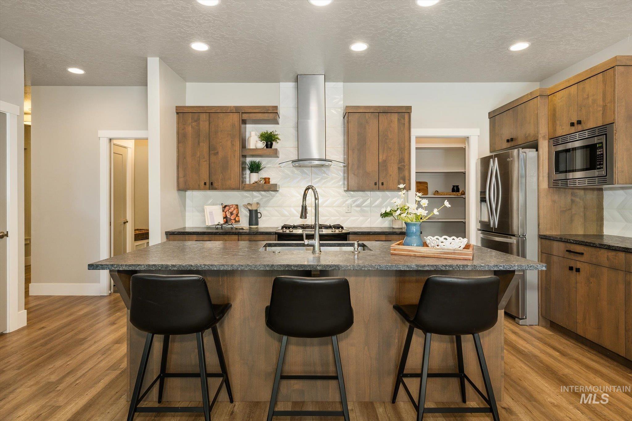 1915 South High Street Boise, ID 83706 - Photo 18 of 44 Kitchen featuring a central island with countertop seating, wood-finish flooring, full height wood cabinetry, stainless steel appliances, and a tile backsplash