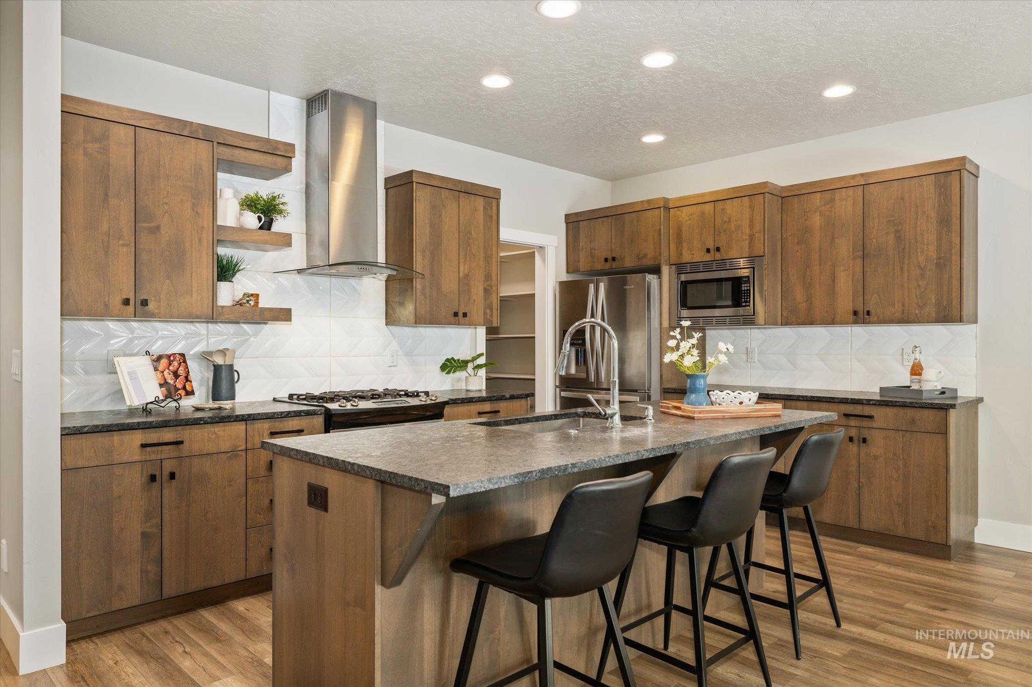 1915 South High Street Boise, ID 83706 - Photo 19 of 44 Spacious kitchen featuring wood-finish cabinetry, a large kitchen island with seating, dark stone countertops, stainless steel appliances, and a chevron pattern backsplash