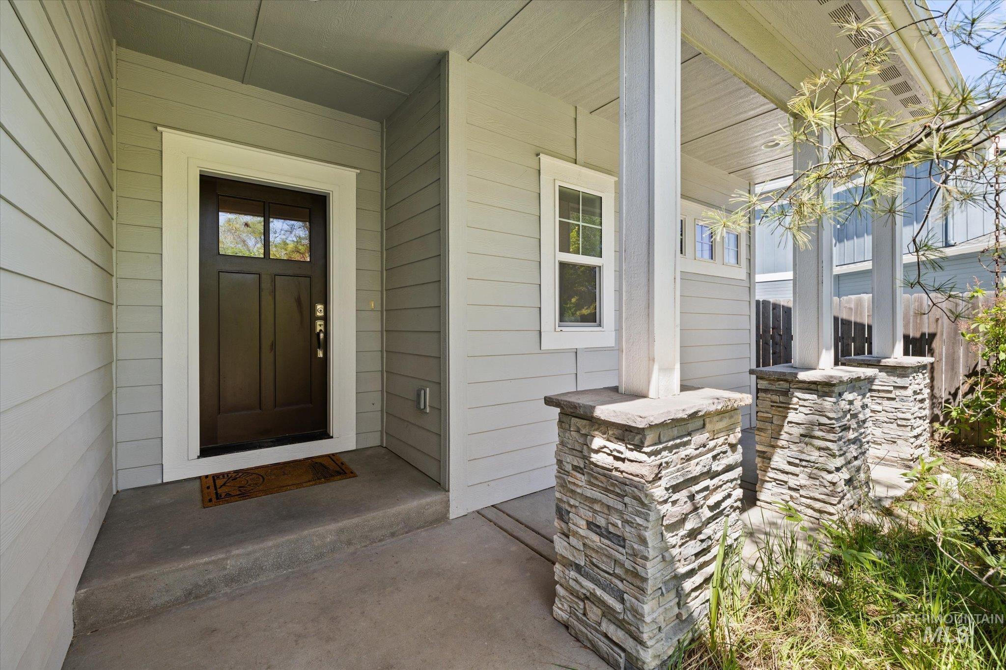 1915 South High Street Boise, ID 83706 - Photo 2 of 44 Covered front porch featuring stacked stone pillar bases, white support columns, light gray siding, and a dark wood-finish entry door with clear glass lites