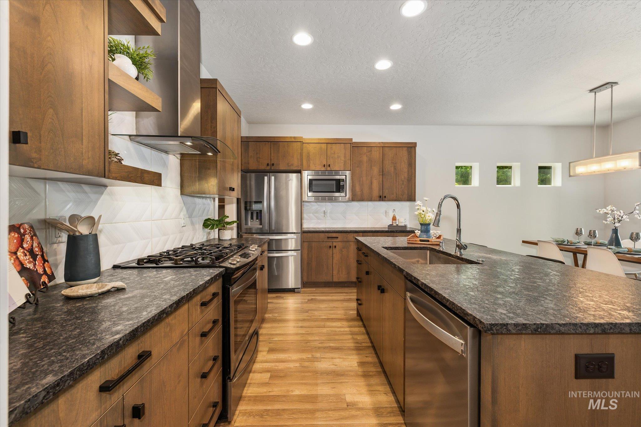 1915 South High Street Boise, ID 83706 - Photo 22 of 44 Modern kitchen featuring wood-finish cabinetry, dark stone-finish countertops, stainless steel appliances, a gas range with a stainless steel vent hood, and a large island with an undermount sink