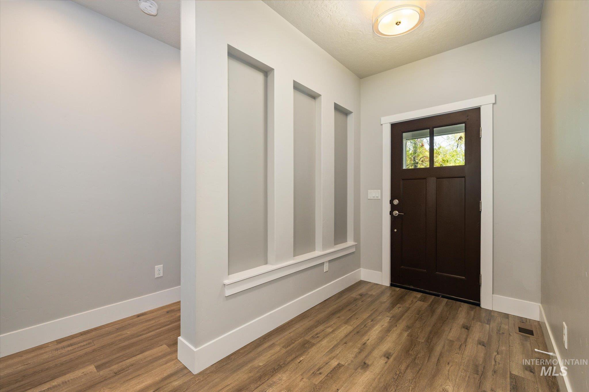 1915 South High Street Boise, ID 83706 - Photo 3 of 44 Entryway featuring wood-finish flooring, a contemporary flush-mount ceiling light, a dark wood-paneled door with upper glass panes, and an accent wall with vertical recessed panels and white trim