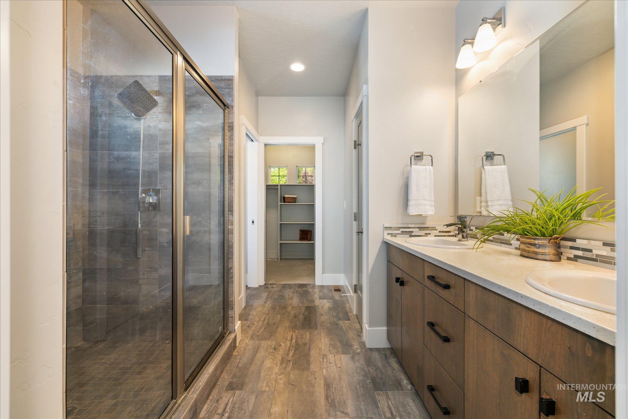 1915 South High Street Boise, ID 83706 - Photo 6 of 44 Spacious bathroom featuring wood-finish flooring, a glass-enclosed shower with dark tile surround, a dual vanity with light countertops, and a tiled backsplash