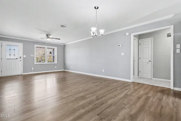 an empty room with wooden floor chandelier and windows