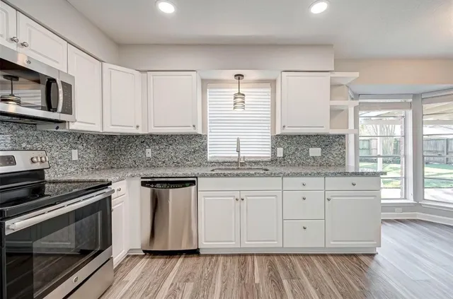 a kitchen with granite countertop white cabinets stainless steel appliances a sink and window