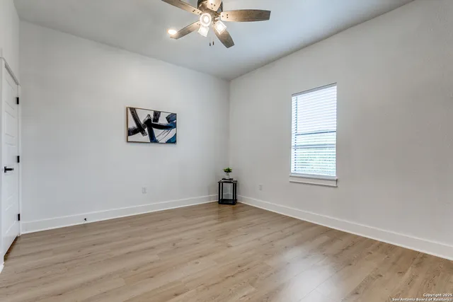 an empty room with wooden floor chandelier fan and windows