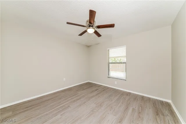 an empty room with wooden floor ceiling fan and windows