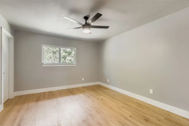 an empty room with wooden floor fan and windows