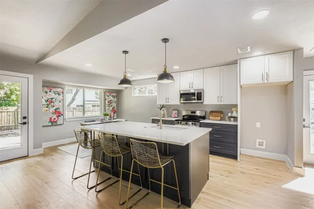 a kitchen with stainless steel appliances a stove a sink a refrigerator white cabinets and wooden floor