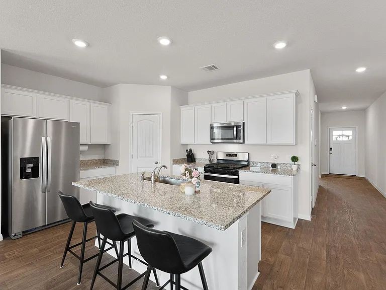 305 Evergreen Sumac Loop Kyle, TX 78640 - Photo 7 of 29 a kitchen with stainless steel appliances granite countertop a kitchen island hardwood floor sink stove refrigerator and microwave
