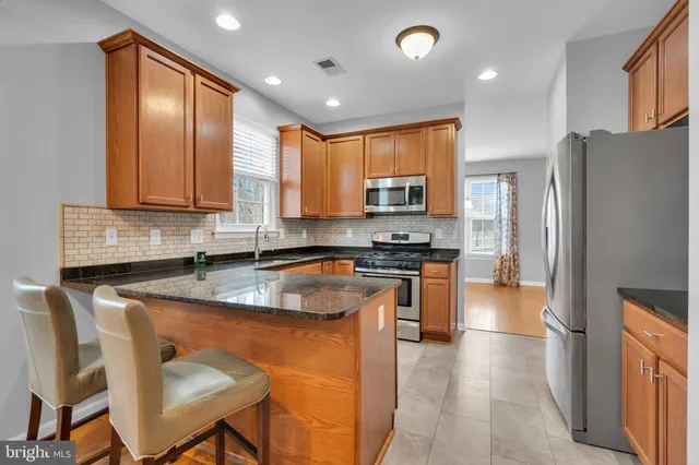 a kitchen with stainless steel appliances granite countertop a stove top oven a refrigerator a sink a dining table and chairs