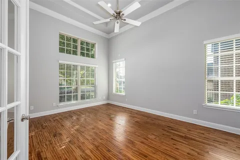 an empty room with wooden floor fan and windows