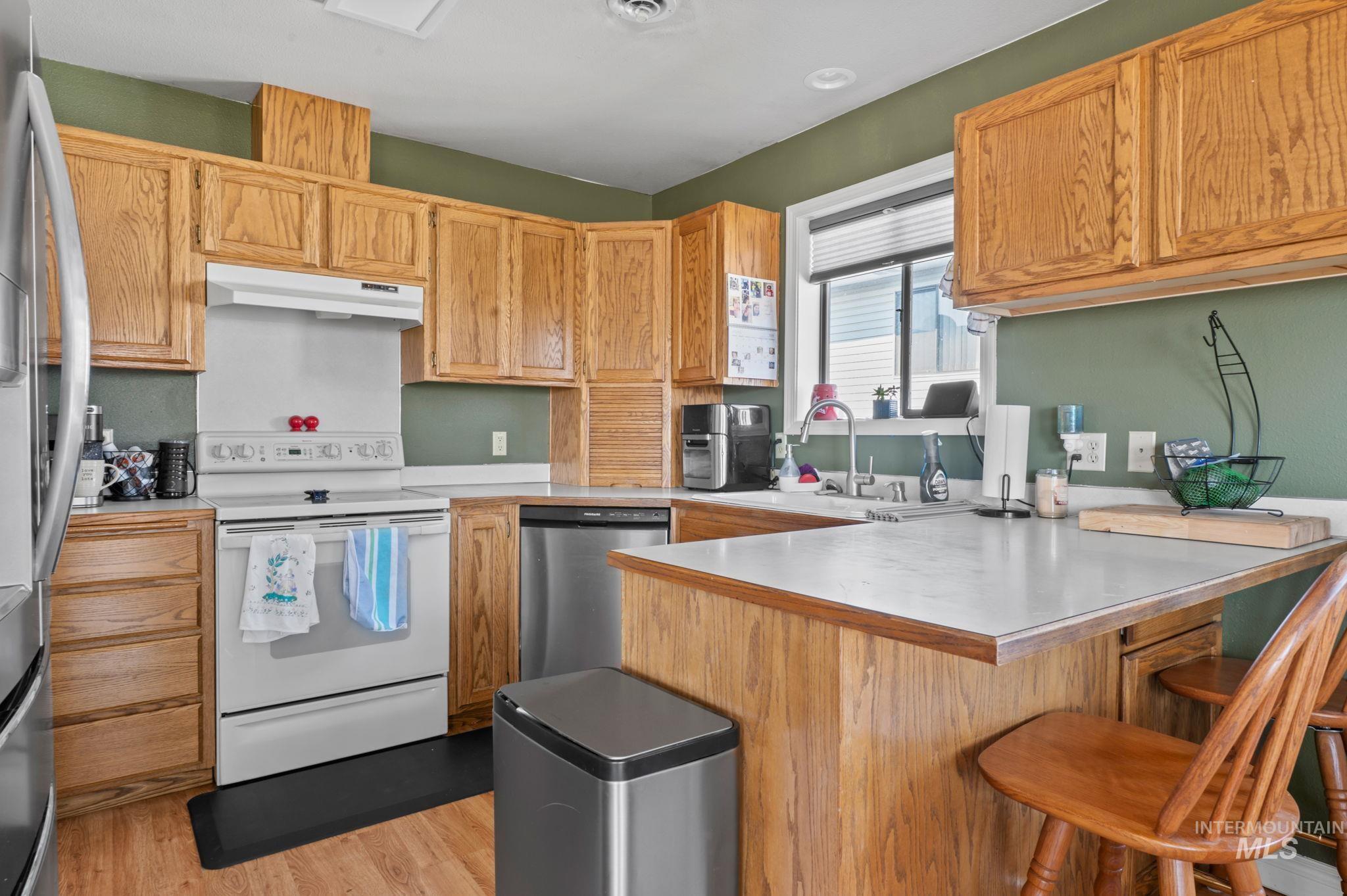 1443 29th Street Lewiston, ID 83501 - Photo 7 of 26 Kitchen with appliances with stainless steel finishes, under cabinet range hood, a peninsula, light countertops, and a breakfast bar