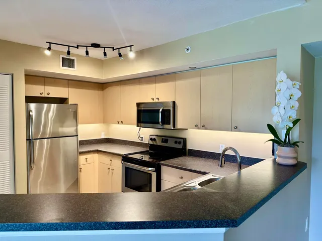 a kitchen with stainless steel appliances granite countertop a refrigerator a sink dishwasher a stove and a dining table with wooden floor