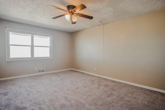 an empty room with a chandelier fan and windows