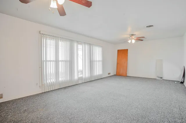 an empty room with chandelier fan and windows