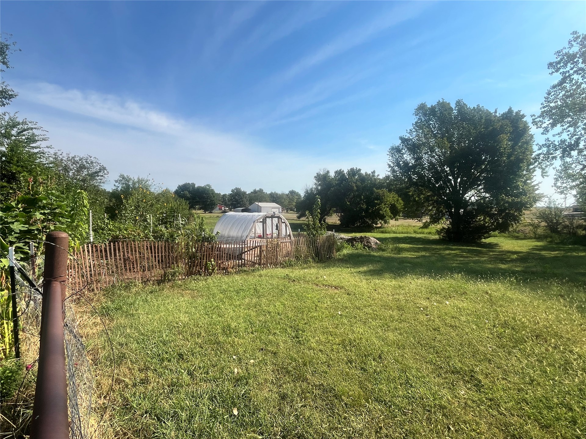 11131 215th Road Nowata, OK 74048 - Photo 36 of 47 Expansive grassy area featuring a greenhouse structure, a rustic wooden fence, and mature trees