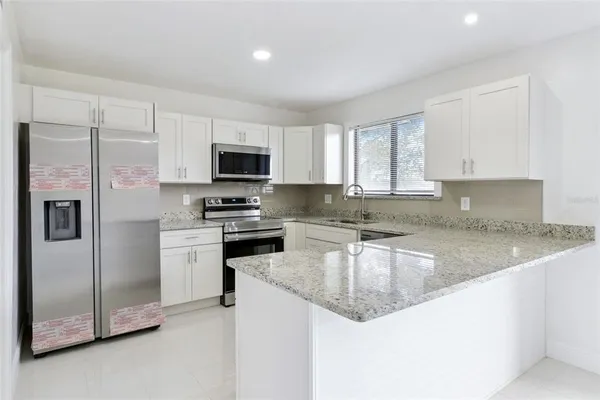 a kitchen with granite countertop a refrigerator a sink a stove a microwave and cabinets