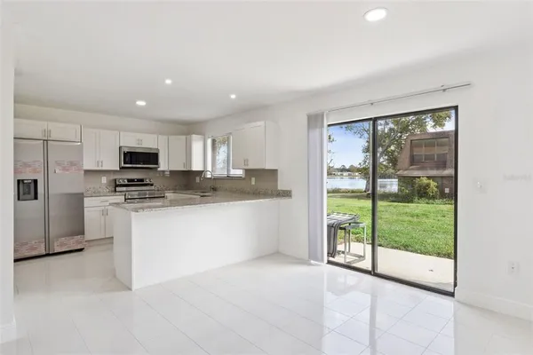 a large white kitchen with granite countertop a refrigerator a stove a sink and a large window