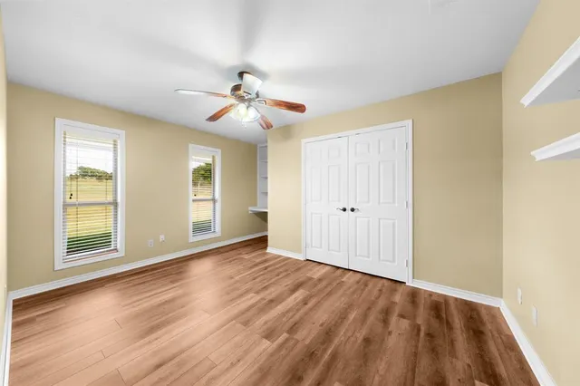 a view of an empty room with wooden floor and a ceiling fan
