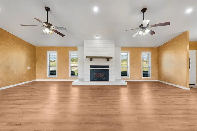 a view of an empty room with wooden floor fireplace and a window