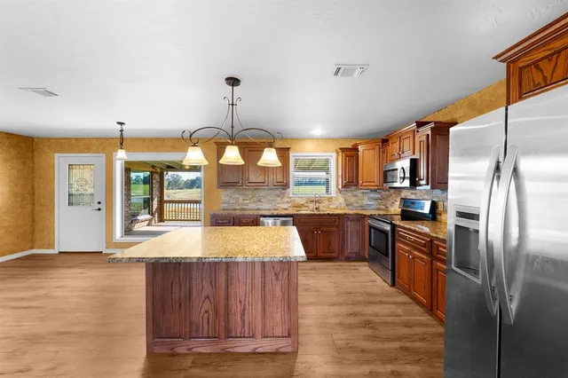 a large kitchen with stainless steel appliances kitchen island granite countertop a refrigerator a sink and wooden cabinets