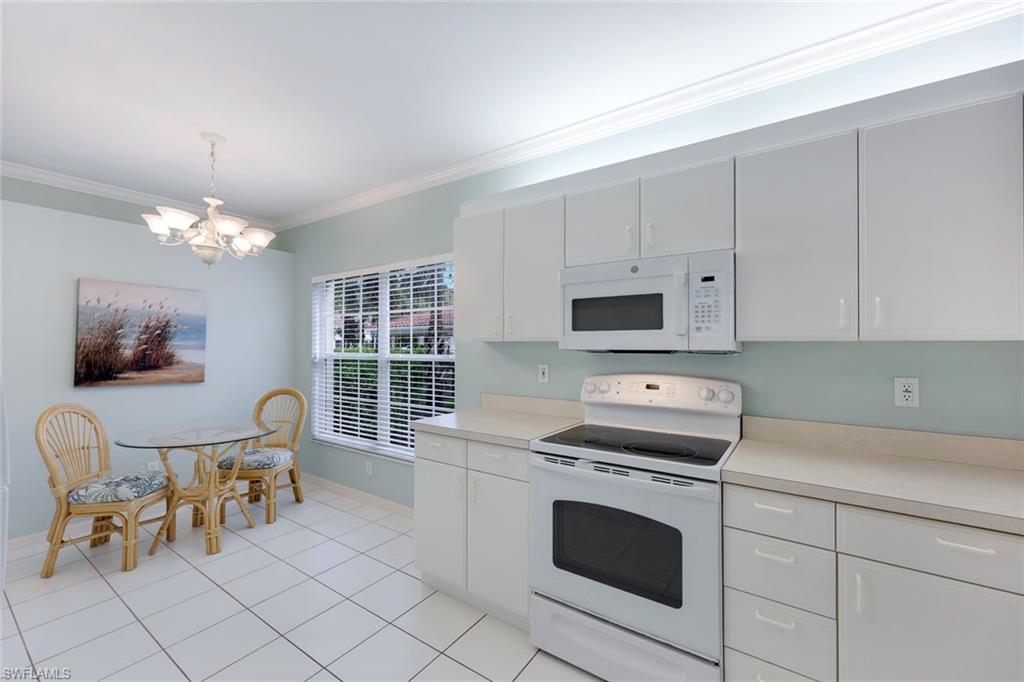 23711 Old Port Road, Unit 101 Estero, FL 34135 - Photo 8 of 30 Kitchen featuring ornamental molding, white cabinetry, a notable chandelier, hanging light fixtures, and white appliances