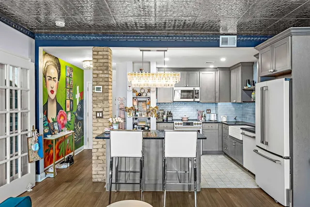 a kitchen with stainless steel appliances granite countertop a refrigerator a stove top oven a dining table and chairs with wooden floor