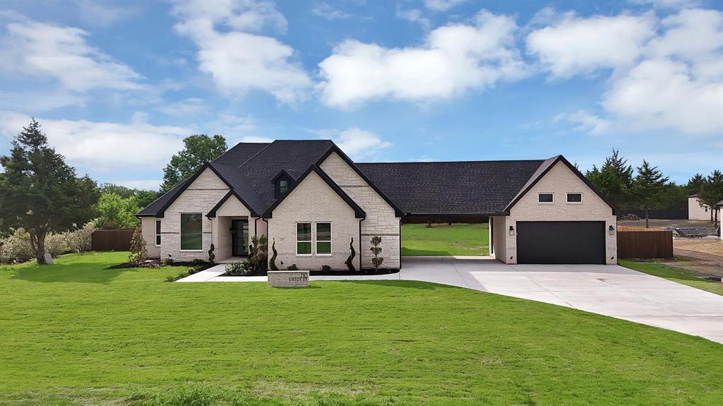 The property features an extensive lawn, a light brick exterior, a dark shingled roof, and a concrete driveway leading to a dark garage door