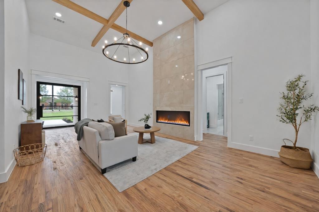 710 Gibson Road Waxahachie, TX 75165 - Photo 4 of 36 Living area featuring hardwood floors, a vaulted ceiling with exposed beams, a modern fireplace with a tiled surround, and a large glass door providing natural light