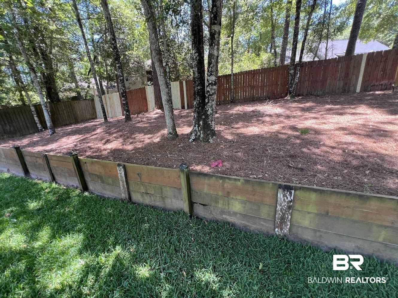 266 Ridgewood Drive Daphne, AL 36526 - Photo 33 of 34 Tiered landscaping featuring a wood retaining wall and a sloped, mulched area with mature trees