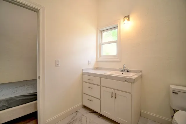 a bathroom with a granite countertop sink a toilet and with a window