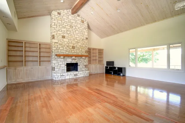 an empty room with wooden floor fireplace and windows