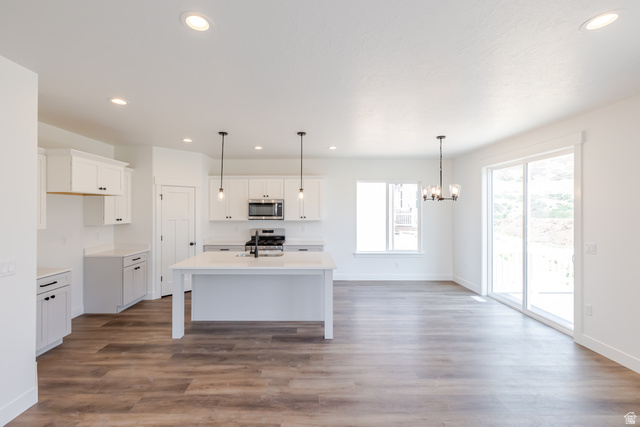 195 West Harmony Rdg Parkway, Unit 601 Mapleton, UT 84664 - Photo 4 of 23 Open-concept kitchen and dining area featuring wood-finish flooring, white cabinetry, a center island with sink, stainless steel appliances, and abundant natural light from a large window and sliding glass door