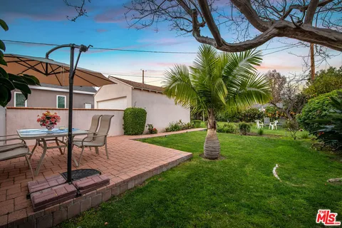 a view of a backyard with table and chairs potted plants and palm trees