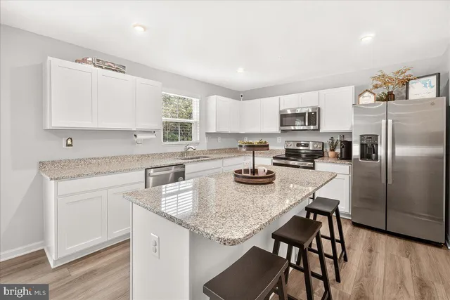 a kitchen with kitchen island granite countertop stainless steel appliances cabinets a sink and a refrigerator