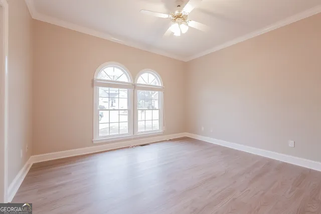 an empty room with wooden floor chandelier fan and windows