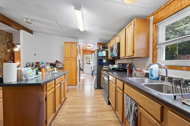 a kitchen with stainless steel appliances granite countertop a sink stove cabinets wooden floor and a window