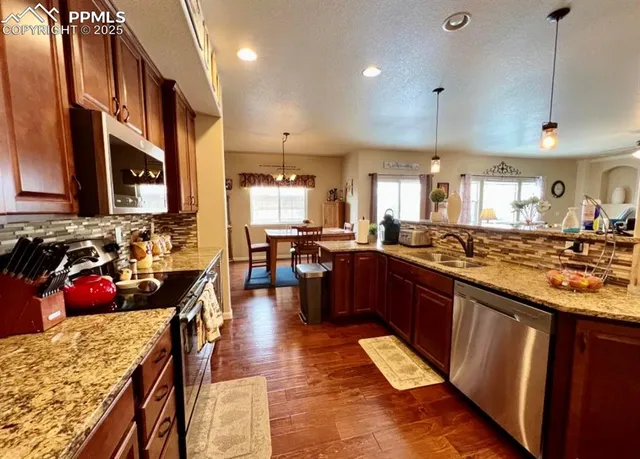 a kitchen with stainless steel appliances granite countertop a refrigerator a stove and a sink with wooden floor