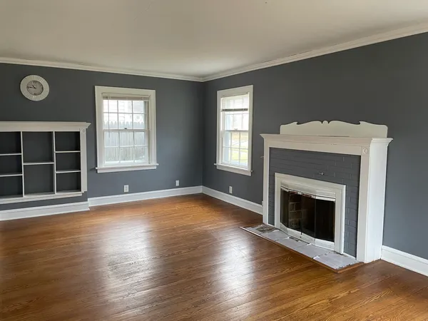 an empty room with wooden floor a fireplace and windows