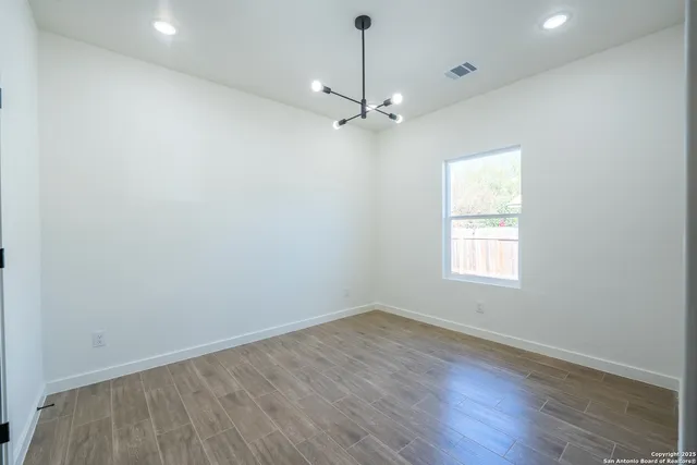 an empty room with wooden floor chandelier fan and windows