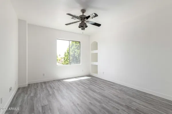 an empty room with wooden floor chandelier fan and windows